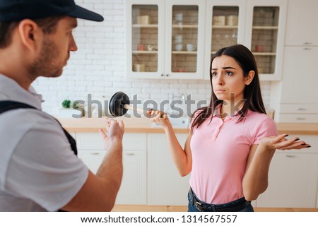 Frustrated confused young woman standi n kitchen and hold hangout. She look upset on plumber. Problem. Need repair. Guy point on sink. Foto stock © 