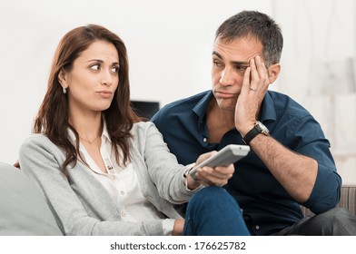 Frustrated Couple Looking At Each Other While Watching Television Sitting On Couch