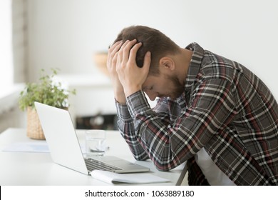 Frustrated depressed man holding head in hands shocked by bankruptcy stock downfall sitting at work desk with laptop, stressed tired businessman feels despair lost money online or got problem debt