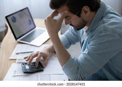 Frustrated depressed stressed young man calculating domestic expenses, having financial problems, considering bank debt, planning mortgage payments, feeling lack of money, bankruptcy concept.