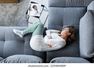 Frustrated depressed young woman lying on couch, drowsing, feeling stress or suffering from abdominal pain. Depression concept. Top view - Powered by Shutterstock