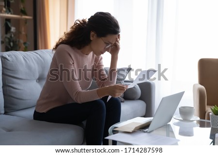Frustrated desperate young woman in eyeglasses touching forehead, looking through banking credit termination, having financial problems, reading refusal document, feeling depressed alone at home.
