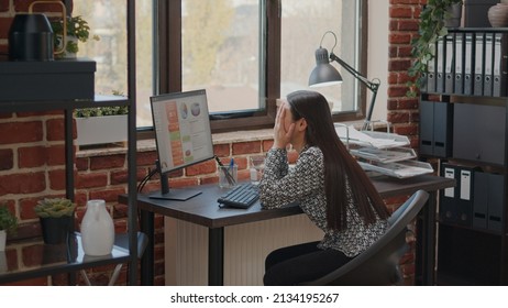 Frustrated employee working under pressure about deadline, using computer to plan business project. Overwhelmed woman feeling burnout at work in company startup office. Tired worker