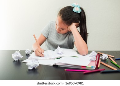 Frustrated and fed up little girl doing his homework. Concept of education and schoolchild. Crumpled pieces of paper on the table.