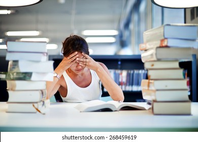 Frustrated Female Student Sitting At The Desk With A Huge Pile Of Study Books In University Library, Young Asian College Student At Hard Exam Preparation In Study Hall Looking Tired And Weary