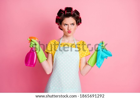 Frustrated girl with hair curlers hold bottle spray rag wear latex gloves isolated on pastel color background