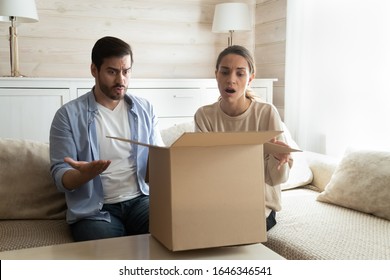 Frustrated Husband And Wife Sit On Couch In Living Room Open Cardboard Package Disappointed With Internet Online Shopping, Confused Upset Young Couple Unpack Parcel Confused With Wrong Order