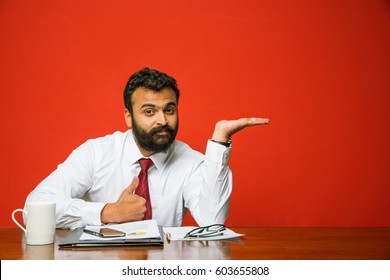 frustrated indian/asian young businessman with beard presenting something while sitting at office desk