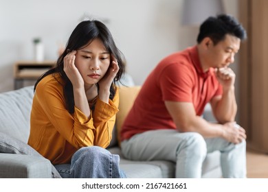 Frustrated japanese spouses after fight, upset asian man and woman sitting on couch far from each other, looking down, thinking about divorce, breakup after quarrel, home interior - Shutterstock ID 2167421661