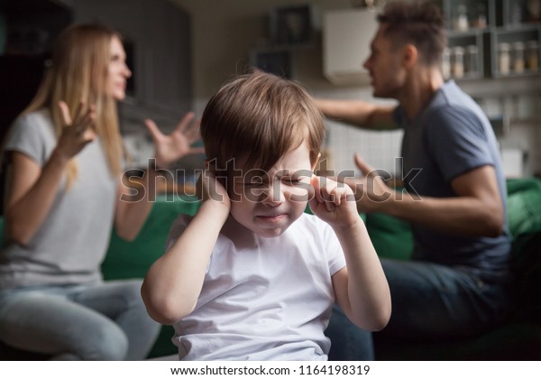 Frustrated kid son puts fingers in ears not\
listening to noisy parents arguing, stressed preschool boy\
suffering from mom and dad fighting shouting, family conflicts\
negative impact on child\
concept