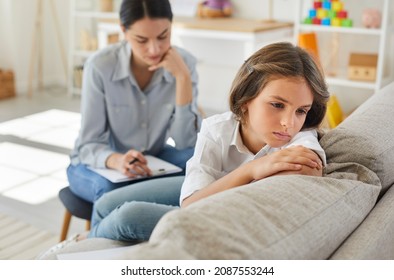 Frustrated little child at psychologist's office. Portrait of girl with sad face sitting on couch during therapy session. Therapist trying to help unhappy, resentful kid who has behaviour issues - Shutterstock ID 2087553244