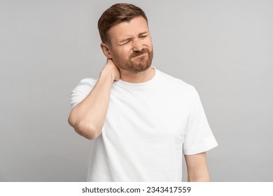 Frustrated man with muscle ache injury have pain in nape. Upset frown guy touches neck suffers from painful feelings ache caused by poor wrong posture sedentary work isolated on studio gray background