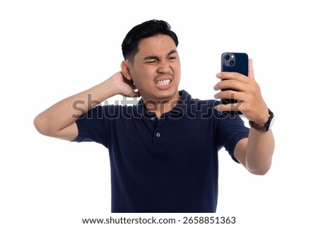 Frustrated man scratching neck while looking at smartphone with confused and annoyed expression isolated on white background