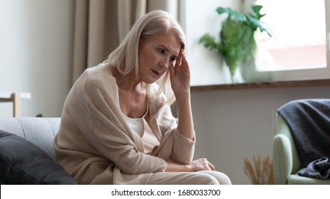 Frustrated Middle Aged Woman Sitting On Couch At Home, Touching Head. Stressed Upset Mature Woman Thinking Of Personal Troubles Or Health Problems. Mental Disorder, Memory Loss, Dementia Concept.