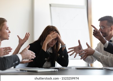 Frustrated millennial female worker sitting at table with colleagues, felling tired of working quarreling at business meeting. Upset stressed young businesswoman suffering from head ache at office. - Shutterstock ID 1523259974