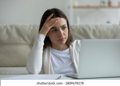 Frustrated millennial woman touching forehead, looking at computer screen, reading banking bankruptcy notification. Unhappy confused young lady feeling shocked about getting email with bad news.