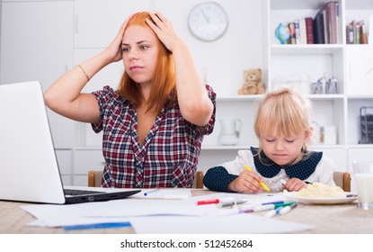 Frustrated Mother Looking In Computer With Daughter Drawing Next To Her 