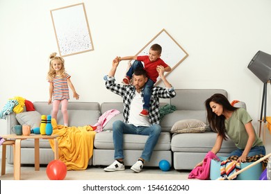 Frustrated Mother Trying To Clean Up Mess While Father Playing With Children In Room