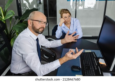 A Frustrated Office Worker Sits At A Table In A Modern Office Space.Portrait Of An Emotional Business Man Looking Away. Sad Business Partners In The Workplace. The Focus Is On The Outraged Man.