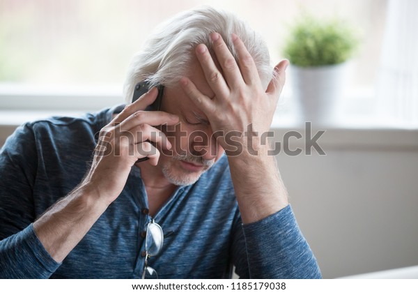 Frustrated older mature retired man feeling upset\
desperate talking on the phone having problems debt, stressed sad\
middle aged male depressed by hearing bad news during mobile\
conversation at home