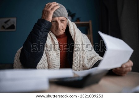 Frustrated poor bankrupt old man freezing at home with no money, holding heating bill, power cut notification letter. Copy space