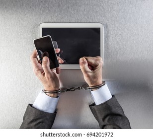 Frustrated Professional Man Hands Tied To Communications Handcuffs Protesting In Using Mobile Phone And Tablet Against The Symbol Of Modern Slavery, Hostage Or Victim Of Business Dependency, Top View