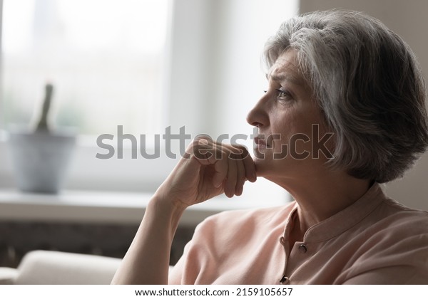 Frustrated sad mature grey haired 50s woman\
thinking over bad news, sitting on couch at home, feeling\
depressed, mourning, going through loss, grief, health problems,\
mental disorder, cancer\
disease