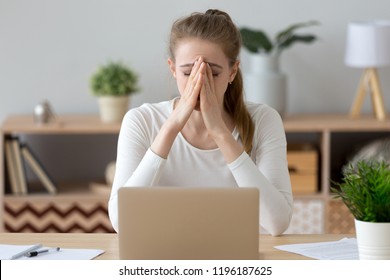 Frustrated sad millennial young woman sitting at the office desk or home. Covering face with hand female worker feels unhealthy headache or eyestrain. Student has a problems receive bad news concept