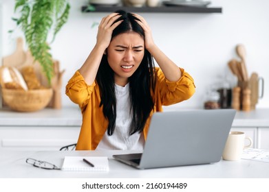 Frustrated sad puzzled Asian brunette girl, freelancer or designer, got a negative result, failed the project, looks desperately at laptop screen, holds her hands on her head, have stressed situation - Shutterstock ID 2160194489
