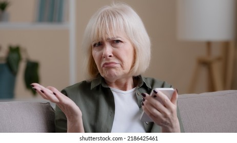 Frustrated Senior Lady Caucasian Elderly Woman With Phone Reads Bad News In Mobile Message Feel Sad Upset Shock Failure With Smartphone App. Worried Mature Female User Customer Lost In Online