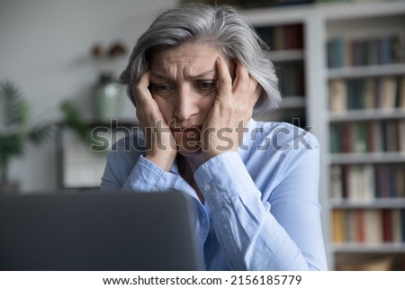 Frustrated senior retired woman touching head, looking at laptop screen with despair, getting bad news, reading online chat message, email letter. Problem with computer concept