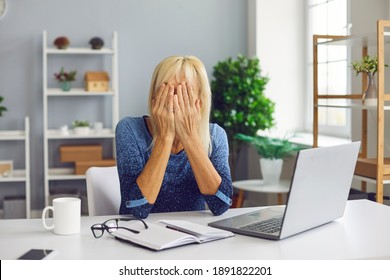 Frustrated Senior Woman Covering Face Unable To Deal With Problem. Online Fraud Victim Scammed On Internet Crying, Sitting At Desk With Laptop Computer. Stressed Mature Lady Having Financial Trouble