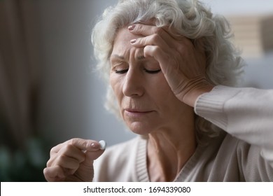 Frustrated Sick Mature Elderly Woman Touching Forehead, Suffering From Strong Migraine Headache, Head Shot Close Up. Worrying Middle Aged Grandmother Feeling Grippe Symptoms, Taking Pills Painkiller.