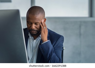 Frustrated stressed business man sitting at desk. Tired mature businessman at workplace with terrible headache. African american boss working at computer with burnout syndrome at desk with copy space.
