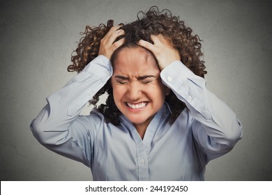 Frustrated stressed young woman. Headshot unhappy overwhelmed girl having headache bad day pulling her hair out isolated on grey wall background. Negative emotion face expression feelings perception 