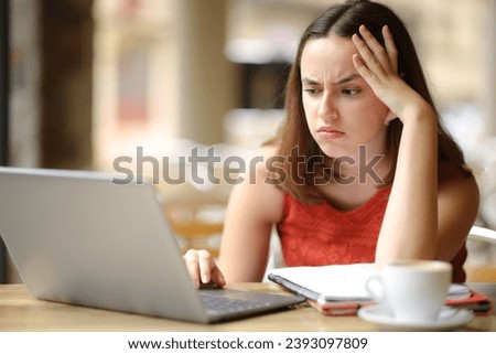 Frustrated student e-learning with a laptop in a restaurant terrace