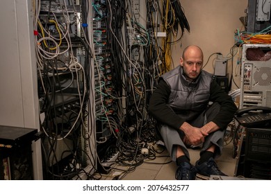 A frustrated technician sits in a server room. A man sits on the floor in a data center among many wires. - Powered by Shutterstock