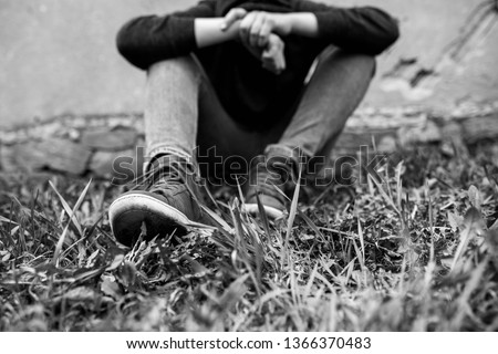 Frustrated teenage boy sitting near a crumbling wall at the correctional institute, focus on the boys shoe, in black and white.