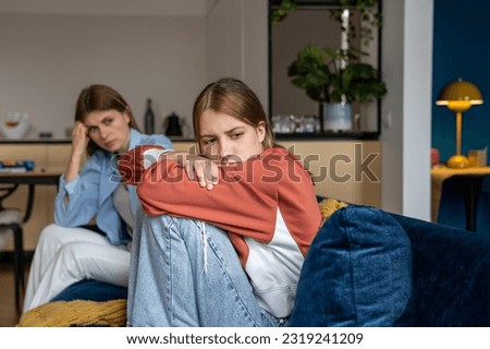 Frustrated teenage girl sits hugging his knees, looks away. Mom sits next daughter and comforts after quarrel. Communication problems between parent and kids.Ignoring children problems.Bulling school