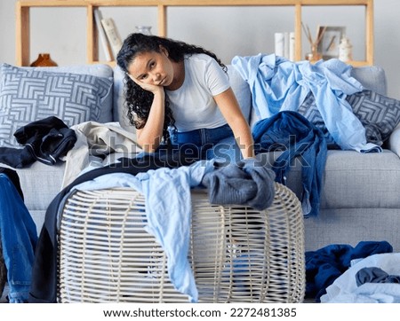 Frustrated, tired and woman with laundry in living room, clothing on floor and sofa, overwhelmed with workload. Stress, burnout and exhausted young housewife sitting on couch with messy apartment.