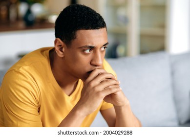 Frustrated Unhappy Latino Millennial Guy In A Yellow T-shirt, Sitting On The Sofa In The Living Room, He Has Personal Problems, Failure At Work, Depression, Bad Mood, Bad News, Sad Young Man Is Lonely