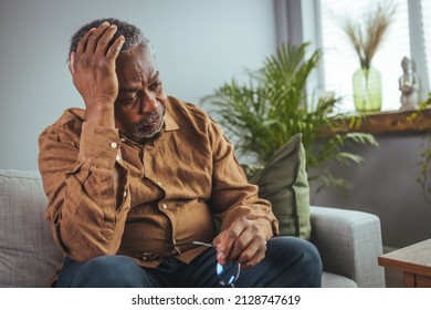 Frustrated Unhealthy Senior Mature Man Touching Head, Having Painful Feelings Sitting Alone At Home. Unhappy Middle Aged Retired Grandfather Suffering From Headache Disease Indoors.