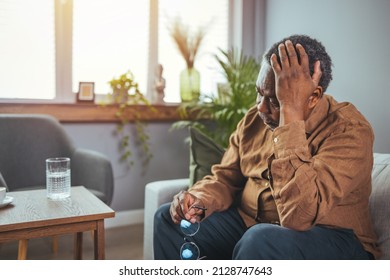 Frustrated Unhealthy Senior Mature Man Touching Head, Having Painful Feelings Sitting Alone At Home. Unhappy Middle Aged Retired Grandfather Suffering From Headache Disease Indoors.