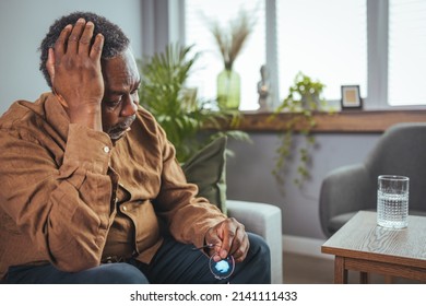 Frustrated Unhealthy Senior Mature Man Touching Head, Having Painful Feelings Sitting Alone At Home. Unhappy Middle Aged Retired Grandfather Suffering From Headache Disease Indoors.