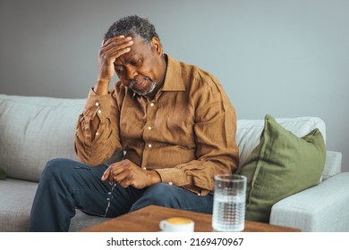 Frustrated Unhealthy Senior Mature Man Touching Head, Having Painful Feelings Sitting Alone At Home. Unhappy Middle Aged Retired Grandfather Suffering From Headache Disease Indoors.