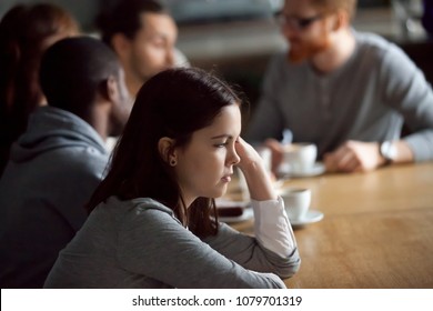 Frustrated upset millennial girl sitting alone at cafe table after conflict ignoring friends, young woman feeling jealous rejected offended thinking of bad relations with boyfriend in public place