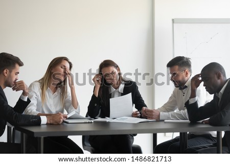 Frustrated upset multiracial business team people sad with bad work result in report disappointed in corporate bankruptcy failure crisis worried of paperwork problem sit at table at office meeting
