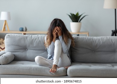 Frustrated woman covering face and crying, sitting on couch at home alone, upset young female suffering from break up with boyfriend or divorce, bad relationship, feeling lonely and depressed