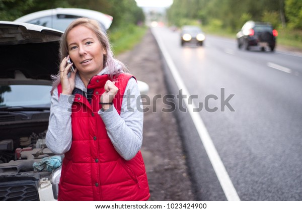 Frustrated woman driver near a broken car.\
A car on a country road, a woman catches a\
ride