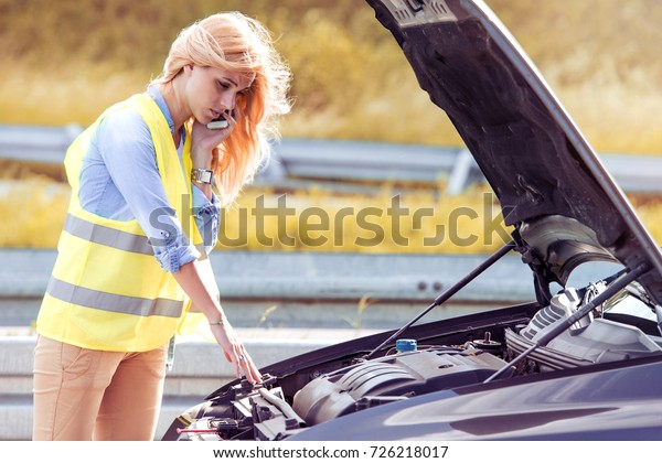 Frustrated woman driver near a broken\
car. Machine on a country road. The woman has\
stress.